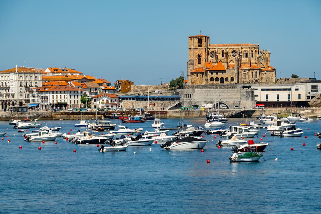 Port de pêche avec bateaux amarrés et église gothique en pierre, village côtier du Nord de l'Espagne